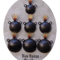 Domovní znamení ve formě plechového oválu se sedmi plastickými symbolickými bombami – 19. století